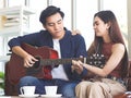 Attractive Asian couple sitting close together on couch in living room , a man playing guitar to his. stay home,stay safe concept Royalty Free Stock Photo