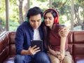 Attractive Asian couple wearing headphones sitting close together on couch in living room at home , man hugging woman , listening Royalty Free Stock Photo