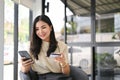 Attractive Asian female holding her smartphone and credit card, using mobile banking app Royalty Free Stock Photo