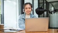 An attractive Asian female radio host is looking at her laptop screen, speaking into a microphone Royalty Free Stock Photo