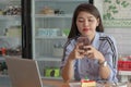 Attractive asian female using a smarphone in a cafe with strawberry cake and laptop