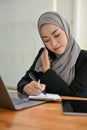 Attractive Asian Muslim businesswoman or secretary taking a notes while talking on the phone Royalty Free Stock Photo