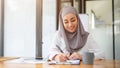 An attractive Asian Muslim businesswoman is filling out forms, signing document at her desk Royalty Free Stock Photo