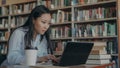 Attractive asian student girl sitting at table with pile of books in university library working on laptop computer Royalty Free Stock Photo