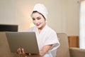 Attractive Asian woman in bathrobe using laptop and appalying facial clay mask on her face at home Royalty Free Stock Photo