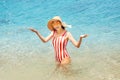 Attractive Asian woman in a closed striped swimsuit is resting on the resort beach on the coast of the calm azure sea Royalty Free Stock Photo