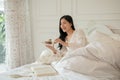 An attractive Asian woman in long dress pajamas is having breakfast in bed