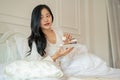 An attractive Asian woman in long dress pajamas is having breakfast in bed