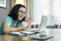 Attractive Asian woman making video call with laptop computer and waving hand. Young female in blue shirt talking with family and Royalty Free Stock Photo