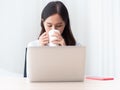 Attractive asian woman sit in front of laptop computer sipping coffee with thoughtfulness. Isolated Royalty Free Stock Photo