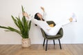 Attractive Asian woman sitting on modern chair and hands up raised arms from happiness in living room Royalty Free Stock Photo