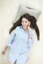 Asian woman speaking on the phone while laying on wood floor. Royalty Free Stock Photo