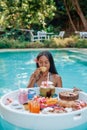 Young asian woman drinks fruit juice swimming in pool with floating table Royalty Free Stock Photo