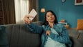 Attractive Asian woman takes a selfie on a smartphone, poses. A young woman is sitting on a sofa in the living room with Royalty Free Stock Photo