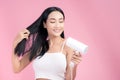 Attractive Asian woman usinf hair dryer on pink background