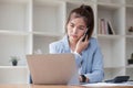 Attractive Asian woman using laptop in online meeting. Businesswoman using mobile phone talking with colleague sitting Royalty Free Stock Photo