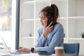 Attractive Asian woman using laptop in online meeting. Businesswoman using mobile phone talking with colleague sitting Royalty Free Stock Photo