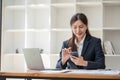 Attractive Asian woman using laptop in online meeting. Businesswoman using mobile phone talking with colleague sitting Royalty Free Stock Photo