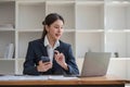 Attractive Asian woman using laptop in online meeting. Businesswoman using mobile phone talking with colleague sitting Royalty Free Stock Photo