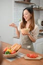 An attractive Asian woman wearing apron, holding a salad bowl, eating salad in her kitchen Royalty Free Stock Photo