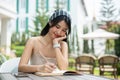 An attractive Asian woman writing her diary at a table in a beautiful garden on a bright day Royalty Free Stock Photo