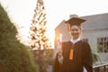 Happy graduated young woman in cap and gown talking with parent in mobile phone and looking certificated in hand so proud Royalty Free Stock Photo