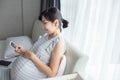 Asian pregnant woman holding and looking at ultrasound photo sitting on bed