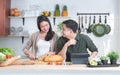 Attractive Asian young sweet couple cooking at home kitchen together. Beautiful wife smiling and slicing bread, enjoy preparing Royalty Free Stock Photo