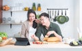 Attractive Asian young sweet couple looking recipe by using tablet at home kitchen, smiling, enjoy cooking preparing healthy Royalty Free Stock Photo