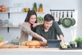 Attractive Asian young sweet couple looking recipe by using tablet at home kitchen, smiling, enjoy cooking preparing healthy Royalty Free Stock Photo