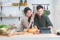 Attractive Asian young sweet couple looking recipe by using tablet at home kitchen, smiling, enjoy cooking preparing healthy Royalty Free Stock Photo