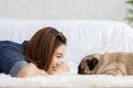 Attractive Asian young woman lying and looking face to face and smile with her dog pug breed in cozy bedroom Royalty Free Stock Photo