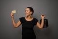Attractive astonished mixed race beautiful woman poses against gray wall background with a shopping packet and rejoices looking at