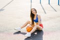 Attractive athletic young woman outdoor posing sitting on basketball court holding basketball Royalty Free Stock Photo