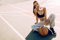 Attractive athletic young woman outdoor posing sitting on basketball court holding basketball Royalty Free Stock Photo