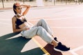 Attractive athletic young woman posing outdoors sitting on basketball court in the morning leaning on basketball. Fashion Royalty Free Stock Photo