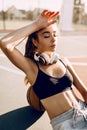 Attractive athletic young woman posing outdoors sitting on basketball court in the morning leaning on basketball. Fashion Royalty Free Stock Photo