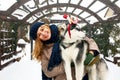 Attractive authentic caucasian woman hugs funny malamute dog wearing santa dear christmas antlers. Curly smiling female