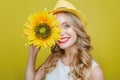 Attractive and awesome young woman is holding a sun flower close to her face. She is looking to camera and smiling. This