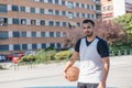 Attractive basketball player looks at camera smiling while posing with his ball on an urban court