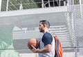 Attractive basketball player walks beside a metal wall carrying his backpack and his orange ball