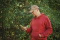 Attractive beard caucasian man in cap and red sweatshort holding smartphone in one hand and reading news or texting