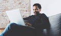 Attractive bearded African man smling and working on laptop while sitting sofa at his modern home office.Concept of Royalty Free Stock Photo