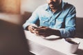 Attractive bearded African man using smartphone while sitting at the wooden table his modern home.Concept of people Royalty Free Stock Photo