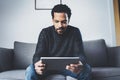 Attractive bearded African man using tablet while sitting on sofa in his modern office.Concept of young business people Royalty Free Stock Photo