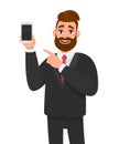 Attractive bearded businessman holding/showing brand new smartphone/mobile/cell phone in hand and pointing index finger towards. Royalty Free Stock Photo