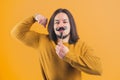 Attractive bearded handsome hispanic boy hanging paper moustache and tighting muscles on a yellow background in a studio