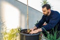 Attractive bearded man in dark clothing transplanting a tomato plant sprout into a larger pot in his urban garden set up on the Royalty Free Stock Photo