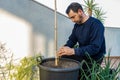 Attractive bearded man in dark clothing transplanting a tomato plant sprout into a larger pot in his urban garden set up on the Royalty Free Stock Photo