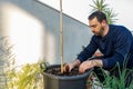 Attractive bearded man in dark clothing transplanting a tomato plant sprout into a larger pot in his urban garden set up on the Royalty Free Stock Photo